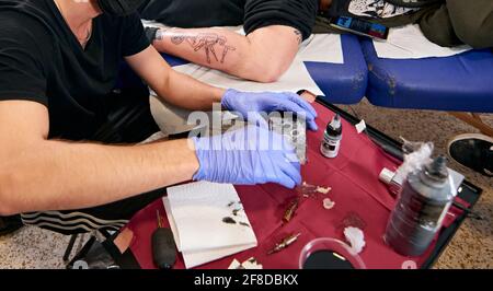 Tätowierer in blauen Handschuhen, die ein Tattoo auf dem machen Bein eines Mannes in einem Studio Stockfoto