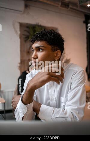 Ein junger schwarzer Mann sitzt mit einem Laptop am Tisch, trinkt Tee und benutzt ein Smartphone. Der Typ im Café. Arbeiten außerhalb des Büros, Remote Stockfoto