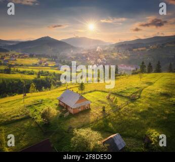 Luftaufnahme des schönen Dorfes in den Karpaten bei Sonnenuntergang im Sommer. Bunte Landschaft mit grünen Wiesen, Häusern mit Gärten, Bäumen, Himmel w Stockfoto