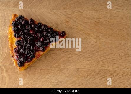 Ein geschnittenes Stück Karottenkuchen, oben mit Johannisbeeren bestreut, liegt von der Seite nach links auf einem Holzbrett Stockfoto