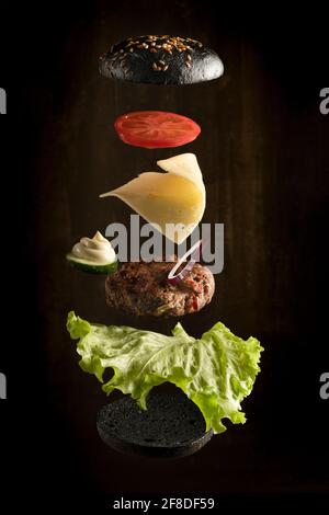 Fliegende Zutaten für hausgemachten Burger auf dunklem Hintergrund Stockfoto