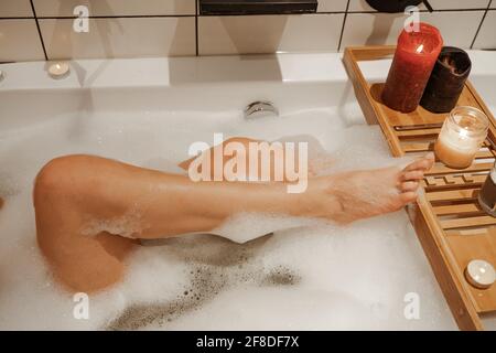 Nahaufnahme des Körpers einer Frau in der Badewanne mit Schaumstoff Und hölzerne Tischvase von Pflanzenkerze Stockfoto