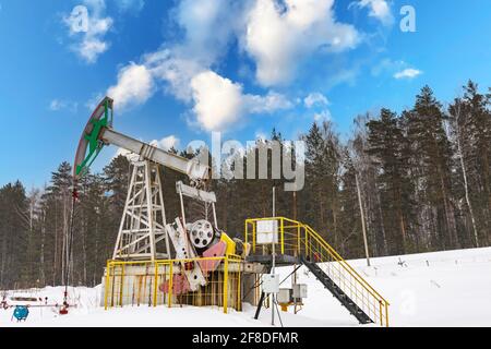 Ölpumpenheber im Winter arbeitet. Am Himmel mit Wolken. Oil Rig Energy Industriemaschine für Erdöl im Sonnenuntergang Hintergrund für Design. Nickend, don Stockfoto