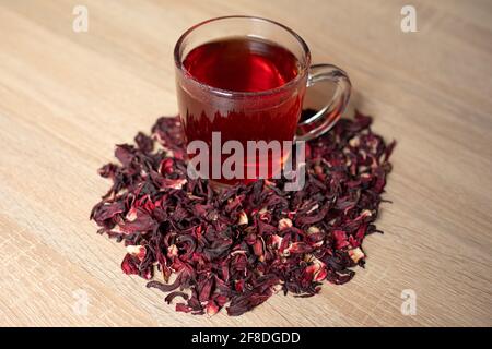 Eine Tasse roten Tee mit Hibiskusblüten auf einem Holztisch Stockfoto