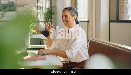 Geschäftsfrau am Schreibtisch, die am Laptop arbeitet und am Smartphone spricht. Frau, die im Büro auf einem Lautsprechertelefon spricht. Stockfoto