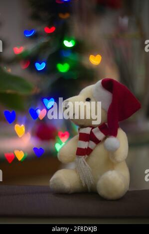 Bild eines Teddybären mit einem typischen Weihnachtshut und roten Tüchern, mit Bokeh von Lichtern in Form eines Herz- und Kopierraums Stockfoto