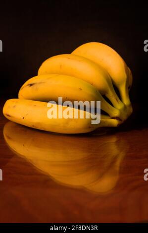 Eine Hand Bananen auf einem dunklen Holztisch, in dem es reflektiert wird, mit dunklem Hintergrund Stockfoto