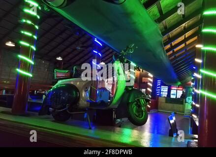 Vintage Retro Zweirad Motorroller geparkt drinnen gegen bunte Lichter in einem anonymen indischen Restaurant Stockfoto