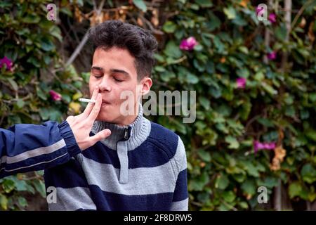 Porträt eines attraktiven hispanischen Mannes, der eine Zigarette raucht Der Park Stockfoto