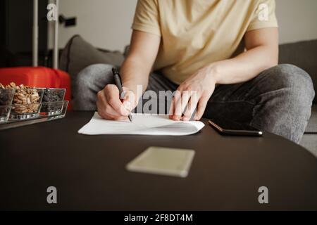 Der junge Reisende sitzt auf der Couch und füllt in den Sommerferien Dokumente im Hotelzimmer aus. Cooler Mann in lässiger Kleidung. Stockfoto