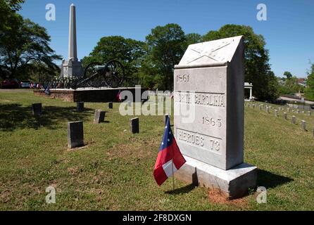 Marietta, GA, USA. April 2021. Denkmäler auf dem Friedhof der Marietta-Konföderierten. Der Marietta Confederate Cemetery ist einer der größten Begräbnisplätze für konföderierte Tote und ist die Ruhestätte für über 3000 Soldaten aus jedem Bundesstaat der Konföderierten sowie aus Maryland, Missouri und Kentucky.Bild: Die ursprüngliche Flagge der Konföderation ist neben einem Denkmal für Soldaten aus North Carolina, die bei Kämpfen in Georgien getötet wurden, zu sehen. Quelle: Robin Rayne/ZUMA Wire/Alamy Live News Stockfoto