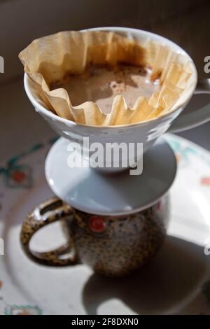 Nahaufnahme eines Guss über Kaffee, der als Wasser eingerichtet wurde Sickert durch gemahlenen Kaffee, und ein Filter tröpfelt hinein Eine Kaffeetasse unten Stockfoto