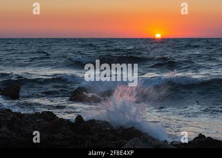 Sonnenuntergang und Sturm auf dem Meer. Große Wellen gegen die untergehende Sonne. Ein Sommersturm im Meer. Schönes Meeresspray mit Schaumbrüchen an der felsigen Küste. Beau Stockfoto