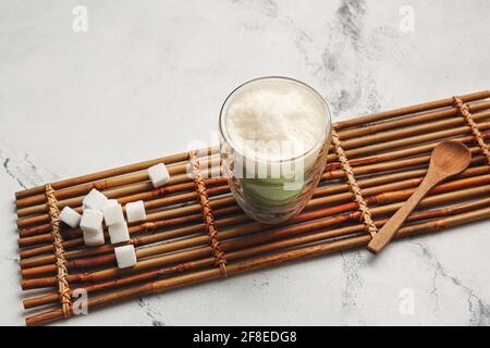 Glas Dalgona Matcha Latte, Zucker und Löffel auf hellem Hintergrund Stockfoto