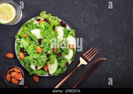 Kalesalat mit getrockneten Preiselbeeren, grünen Äpfeln und Mandeln. Vegan gesundes Essen, Draufsicht, schwarzer Küchentisch Stockfoto