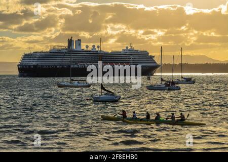 Das Holland Amerika-Kreuzschiff „Noordam“ verlässt den Hafen bei Sonnenuntergang, umgeben von kleineren Booten. Mount Maunganui, Neuseeland Stockfoto