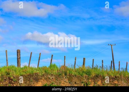 Ein Drahtzaun am Rande einer Farm, mit einem strahlend blauen Himmel und einem Strommast im Hintergrund. Fotografiert in Neuseeland Stockfoto