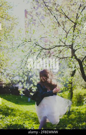 Kleines Mädchen in schwarzer Jacke und weißem Kleid tanzen in Der Kirschgarten im Frühling Stockfoto