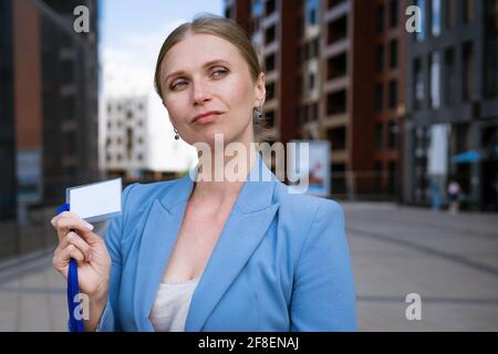 Business stilvolle Frau in einer blauen Jacke hält ein Abzeichen In der Hand vor dem Hintergrund eines Bürogebäudes Stockfoto