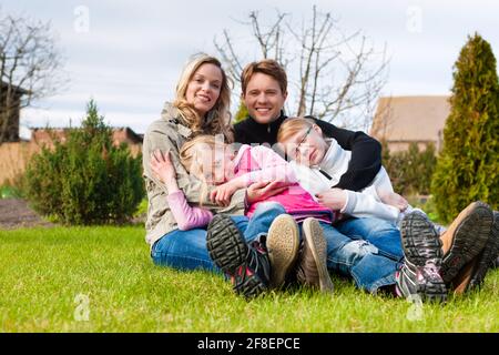 Familie, Vater, Mutter und Töchter, sitzen zusammen auf einer Wiese, sie lachen und Spaß haben Stockfoto