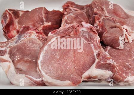 Geschnittenes rohes Schweinekotelett auf weißem Hintergrund. Draufsicht. Flach in weißem Kochgeschirr legen Stockfoto