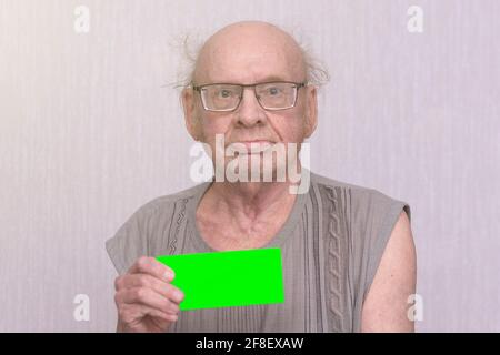 Der alte, pensionierte Glatze mit einer Brille in grauem Hemd liegt leer in der Hand. Stockfoto