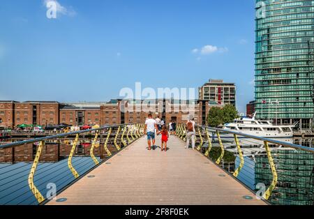London / Großbritannien - 23 2019. August: Die Menschen gehen auf der Fußgängerbrücke North Dock, die das North Dock im Canary Wharf Estate überspannt. Die alten Lagerhäuser von Stockfoto
