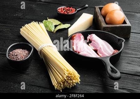 Traditionelle Italienische Pasta Carbonara Zutaten. Speck, Spaghetti, Parmesan und Pecorino-Käse, Ei, Knoblauch-Set, auf schwarzem Holzhintergrund Stockfoto