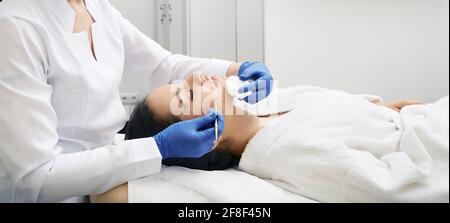 Brunette Frau bekommt mechanische Reinigung Gesichtshaut von Defekten und Entfernung von Mitesser in einer medizinischen Klinik Stockfoto