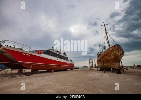 Mangystau, Kasachstan-19. Mai 2012:Bucht von Bautino.Schiffsreparaturwerft am Kaspischen Meer.Altes rostigen Stahlschiff (rechts).Neues rotes Motorboot oder Rettungsboot (links) Stockfoto