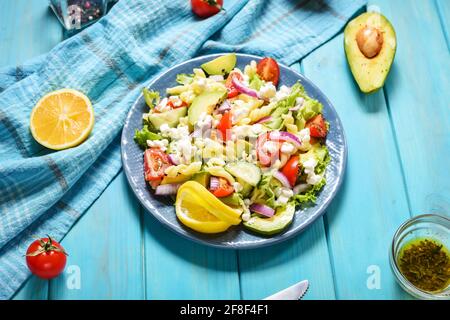 Vegetarisches gesundes Mittagessen - Nudelsalat mit frischem Gemüse, Avocado und Feta auf blauem Holzhintergrund Stockfoto