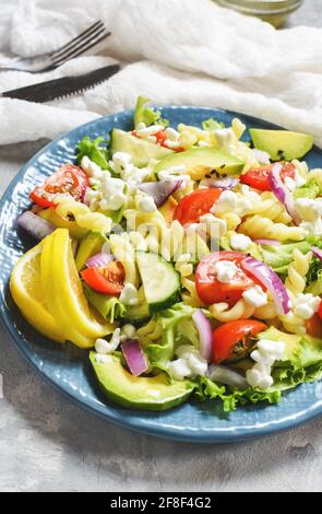 Vegetarisches gesundes Mittagessen - Nudelsalat mit frischem Gemüse, Avocado und Feta auf einem konkreten Hintergrund Stockfoto