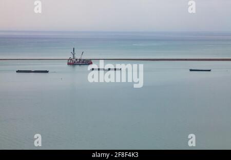 Bucht von Bautino, Kaspisches Meer, Kasachstan. Panoramablick auf die Bucht und den steinernen Pier. Öl-Derrick auf der Wasserplattform. Tankschiffe stehen im Wasser. Stockfoto