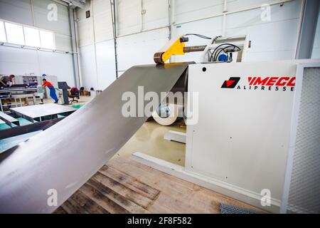 Aktau, Kasachstan. Schneiden von Blech auf der Maschine. Zwei Arbeiter im Hintergrund. Herstellung von speziellen elektrischen Geräten. RIG Ltd Stockfoto