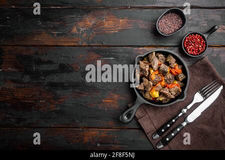 Rindergulasch - rustikales Set, in gusseiserner Bratpfanne, auf altem dunklen Holztisch, Ansicht von oben flach, mit Platz für Text Stockfoto