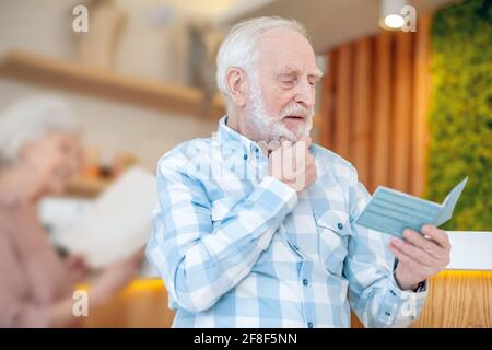 Grauhaariger bärtiger Mann, der etwas liest und dabei aussieht Stockfoto