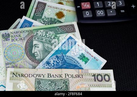 Taschenrechner und polnische Banknoten von 100 PLN und 50 PLN auf schwarzem Hintergrund. Foto aufgenommen unter weichem Kunstlicht Stockfoto