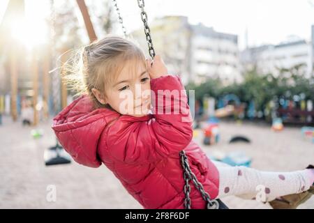 Ein schulpflichtig lächelndes Mädchen, das auf der Fahrt fröhlich lächelt Schaukeln im Park Stockfoto