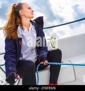 Junge Frau, die ein Segelboot steuert und auf einem See segelt. Sommerferien, Kreuzfahrt, Erholung, Sport, Regatta, Freizeitaktivitäten, Service, Tourismus Stockfoto