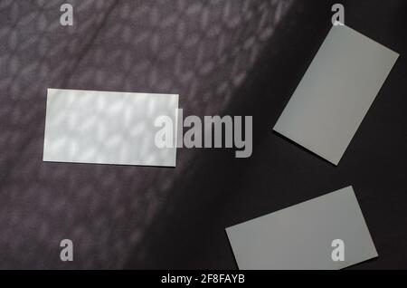 Minimalistische Licht- und Schattenkomposition mit Visitenkarten auf grauem Hintergrund. Drei Rechtecke aus leerem Papier in einem abstrakten Schattenmuster. Diagonale d Stockfoto