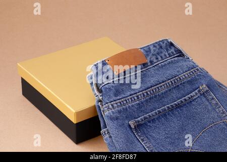 Leeres Etikett oder Etikett aus Leder auf der Gesäßtasche Von blauen Jeans auf einer Vase aus Spulengarn mit Schwarze goldene Schachtel Stockfoto