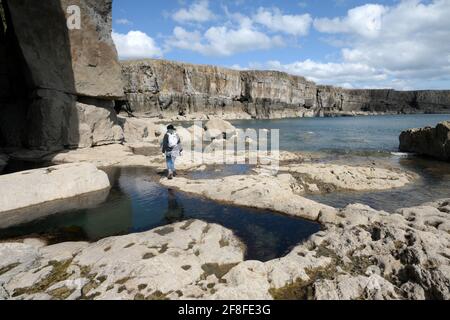 Frau, die auf den Felsenpools am Ufer springt und nach Osten zu St. Govan's blickt Kopf Stockfoto