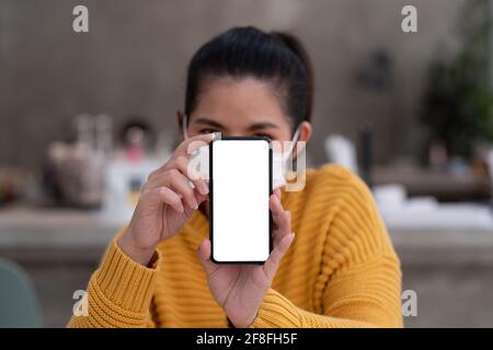 Mockup-Bild einer schönen Frau tragen Maske, während das Mobiltelefon mit leerem weißen Bildschirm halten. Stockfoto