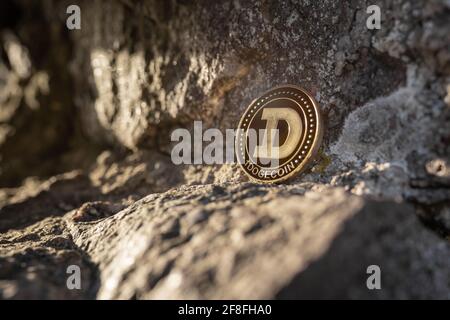 Nahaufnahme von Dogecoin auf einem Stein im Freien mit sanftem Sonnenuntergang Licht auf Felsen Hintergrund mit Kopierfläche. Einzelne physische Metall Gold glänzend Kryptowährung Stockfoto