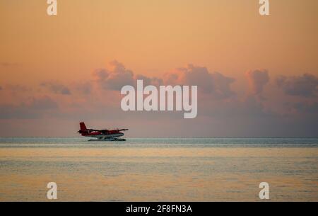 Landung eines Wasserflugzeugs auf der maledivischen Lagune bei Sonnenuntergang. Luxuriöses Reisekonzept Stockfoto