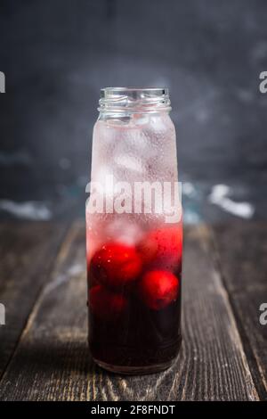 Kirschgetränk mit Beeren und Eis in kleiner Flasche. Selektiver Fokus. Geringe Schärfentiefe. Stockfoto