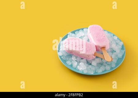 Erdbeerpopsicles und zerkleinertes Eis auf gelbem Hintergrund Stockfoto