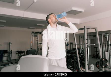 Ein Mann trinkt nach dem Training Wasser aus einem Shaker im Fitnessstudio. Stockfoto
