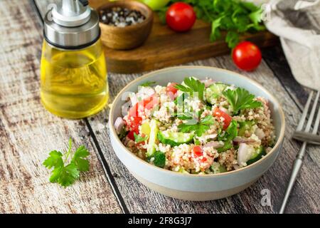 Essen Diät-Konzept, Thunfisch-Salat. Couscous-Salat mit konservierten Thunfisch, Tomaten, Gurken und lila Zwiebeln auf rustikalem Holztisch. Stockfoto