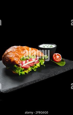 Frisches Croissant-Sandwich mit Fleisch und Gemüse auf schwarzem Hintergrund Stockfoto